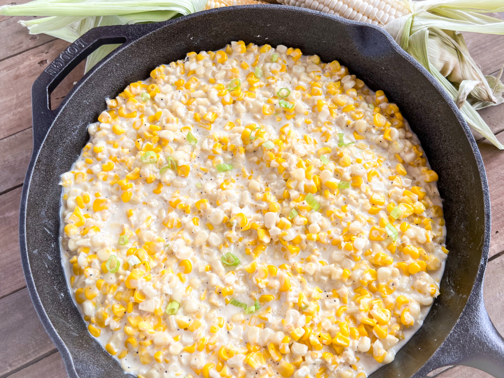 Southern style creamed corn in a cast iron skillet ready to be served with fresh corn in the background.