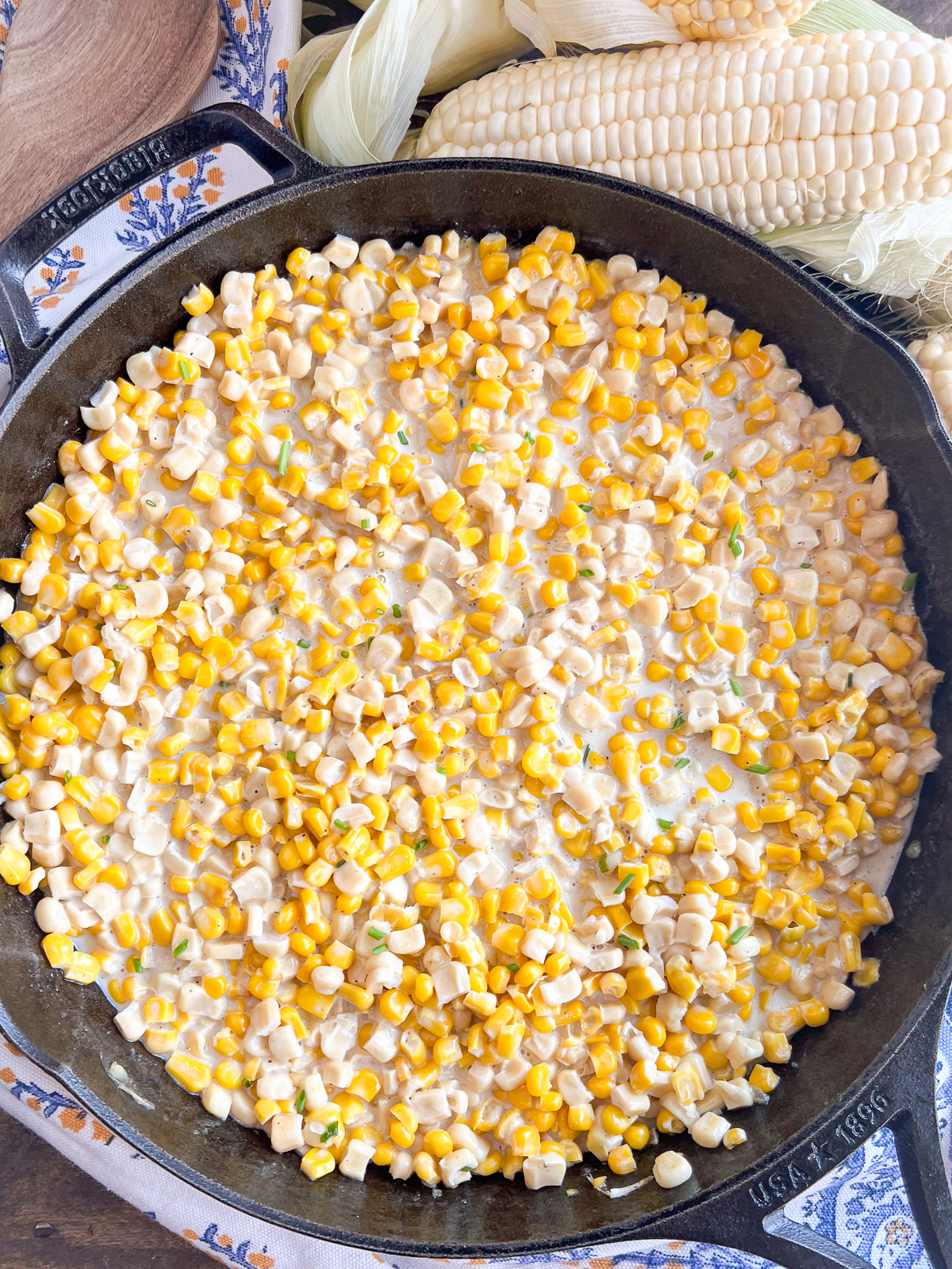 southern style creamed corn in a cast iron skillet with fresh corn on the cob in the background.