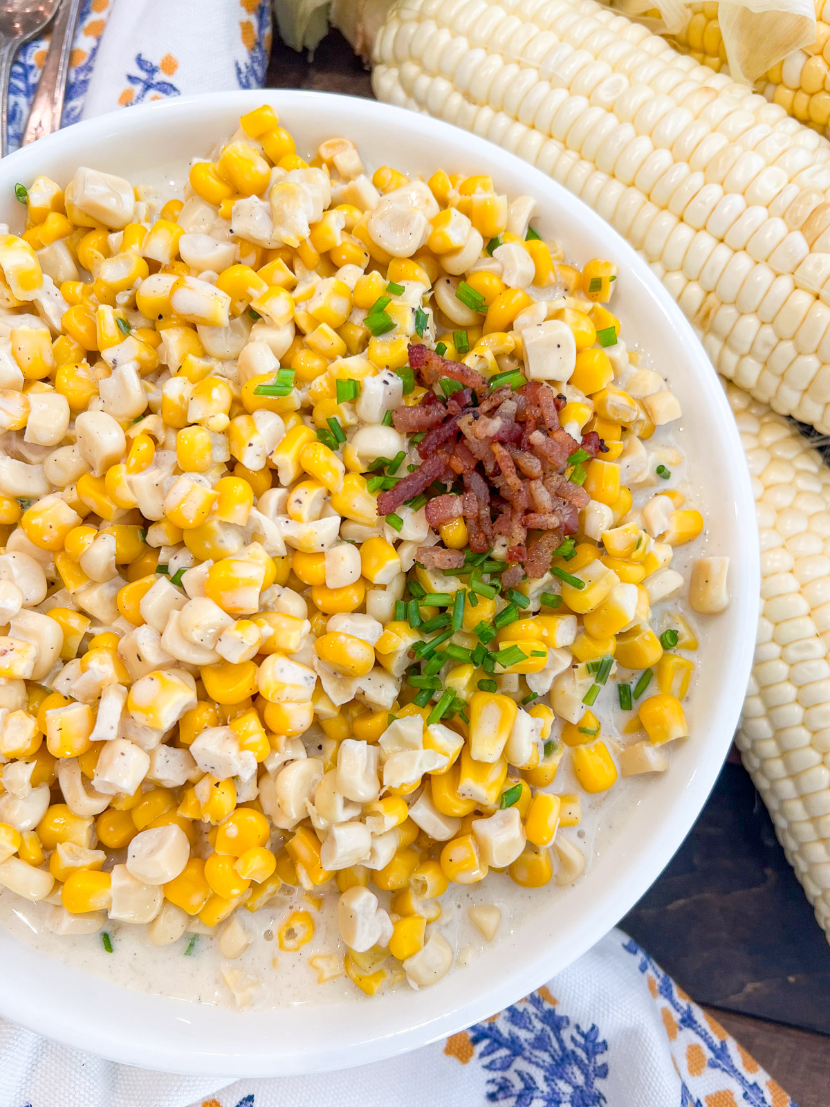 southern creamed corn in a white bowl garnished with chives and bacon crumbles.