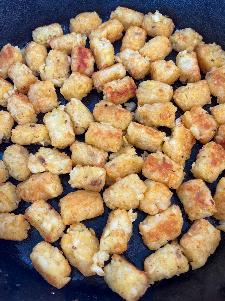 A single layer of crispy tater tots in a cast iron skillet.