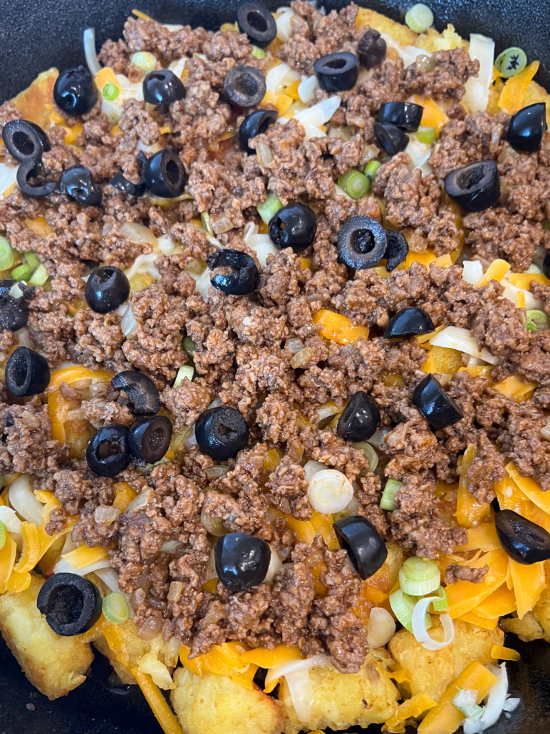 The first layer of totchos has been assembled with the cheeses, seasoned ground beef, green onions, and black olives.