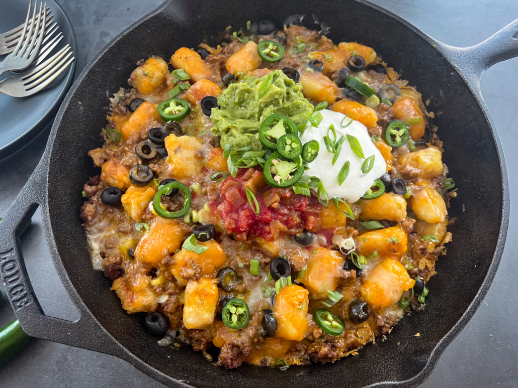 Totchos further garnished with guacamole, salsa, and sour cream.