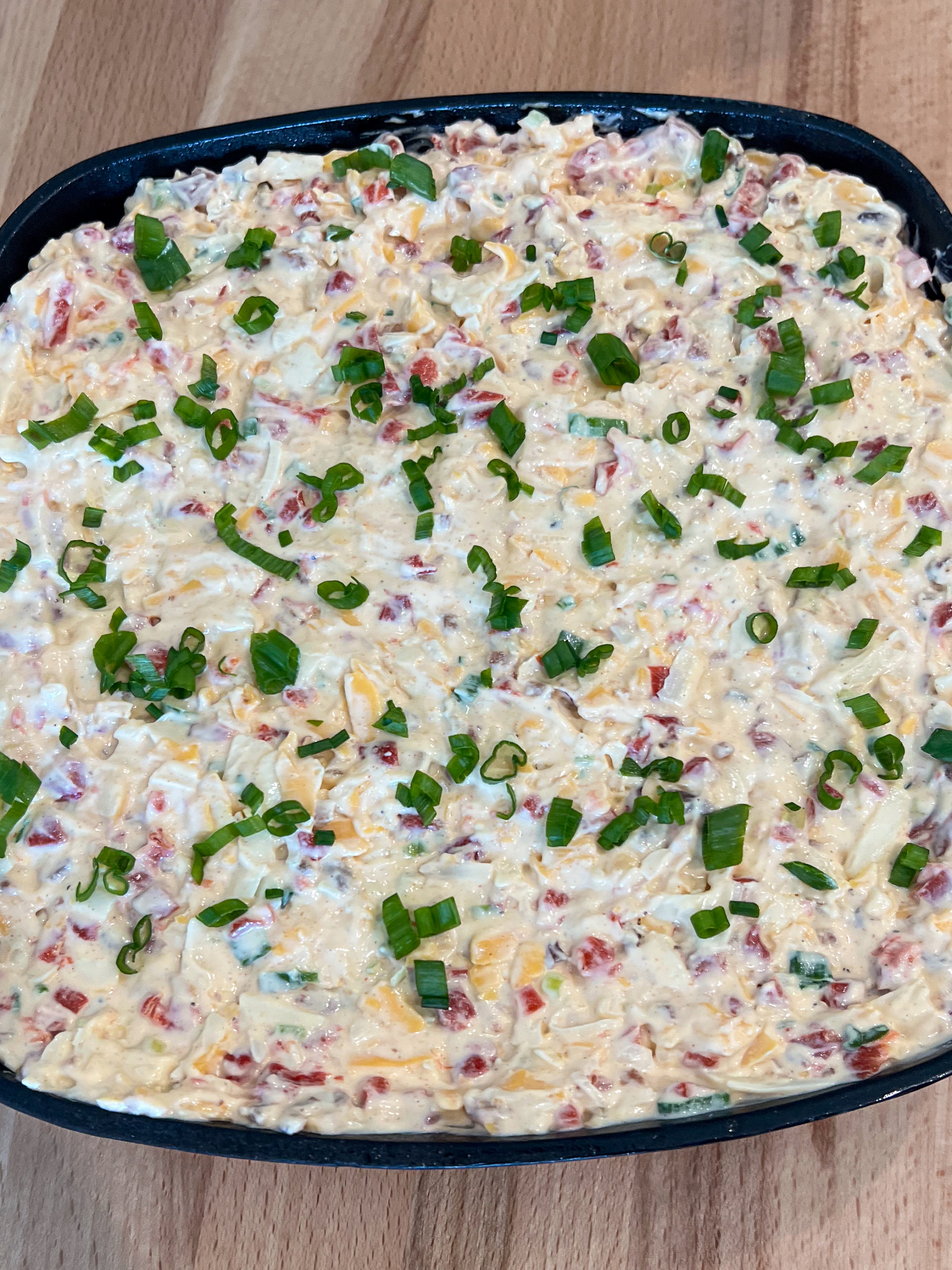 The dip added to a square cast iron skillet and topped with green onions ready to be baked.