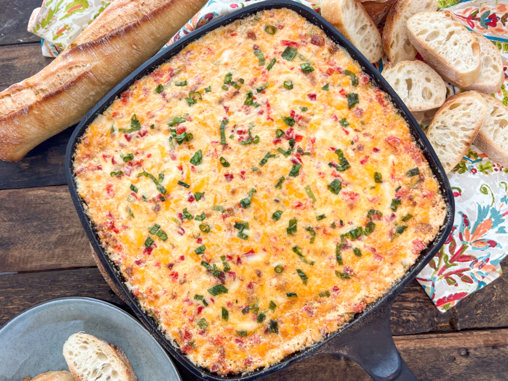 Freshly baked pimento cheese dip still in the skillet with baguette slices around it.