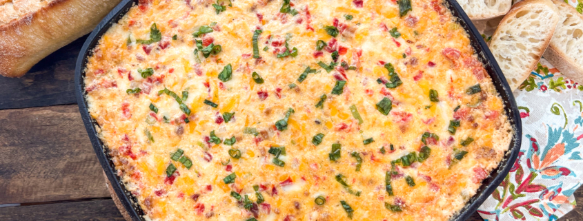 Freshly baked pimento cheese dip still in the skillet with baguette slices around it.