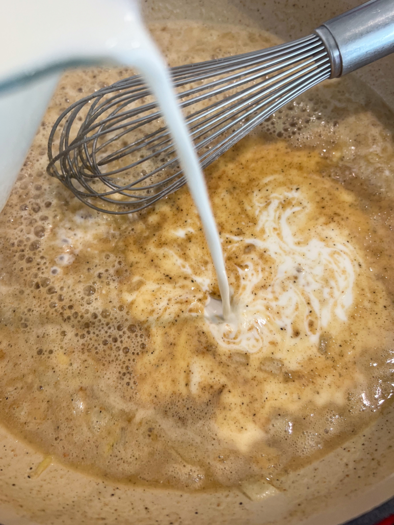 Milk being poured into the roux to form the creamy base for the cheese sauce.