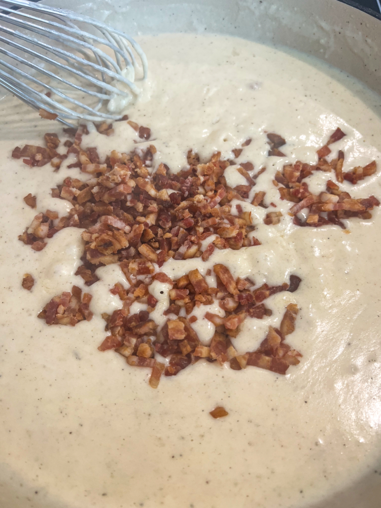 Bacon crumbles being stirred into the cheese sauce.