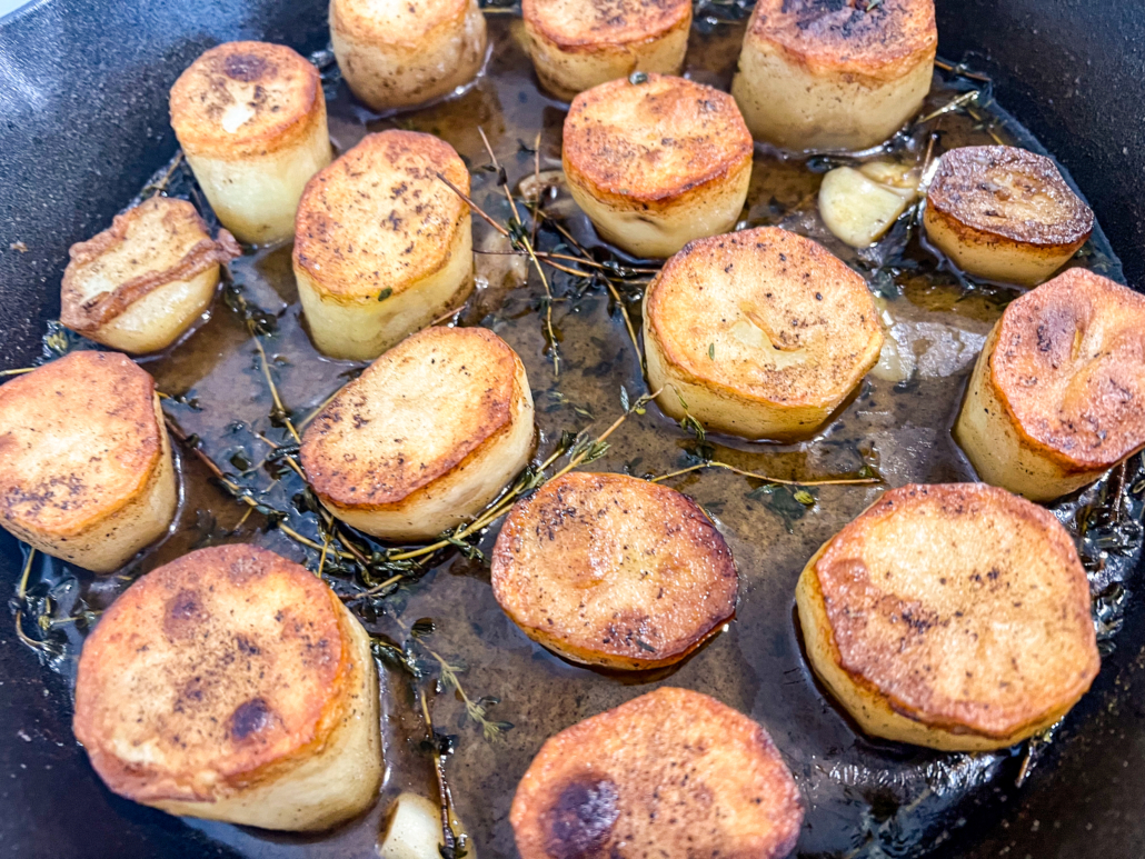 Now fully cooked potatoes still in the cast iron skillet, with the thyme and garlic waiting to be removed and discarded.