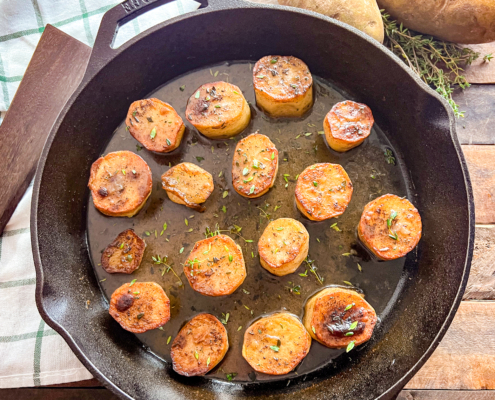Golden brown potatoes in a cast iron skillet sprinkled with fresh thyme.
