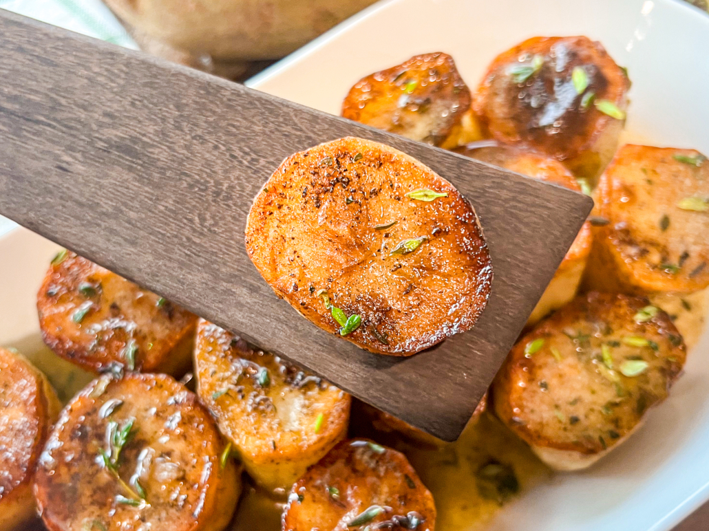 A single melting potato raised above the platter on a wooden spatula.