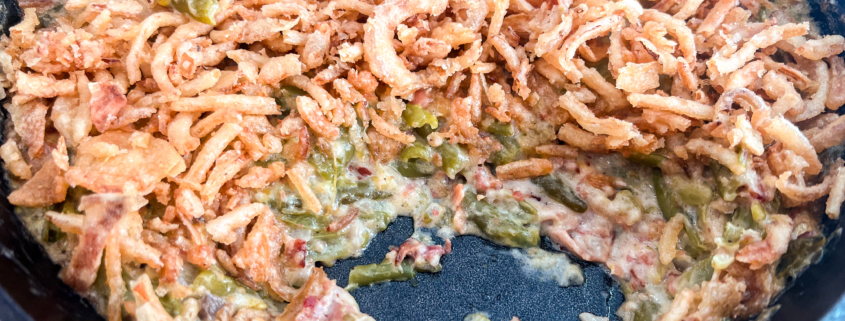 Bacon green bean casserole in a cast iron skillet with a couple portions spooned out.