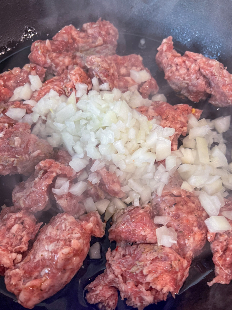 Italian sausage and diced onion being cooked in a cast iron skillet.