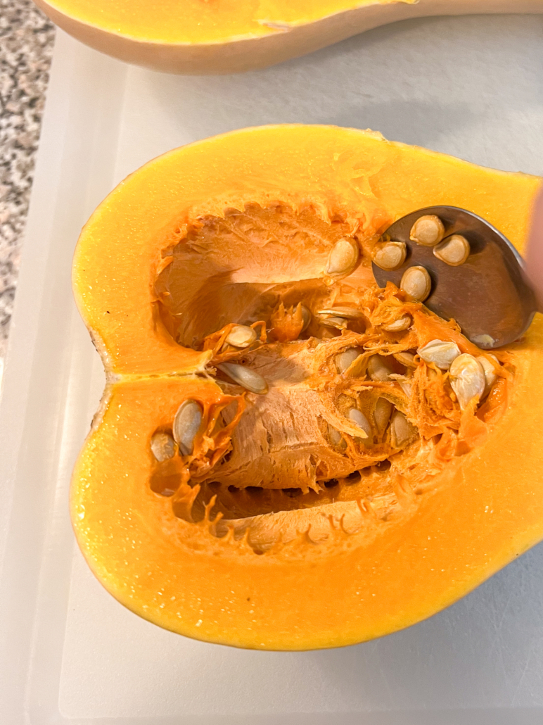 A spoon is being used to scoop out the seeds and pulp of a butternut squash half.