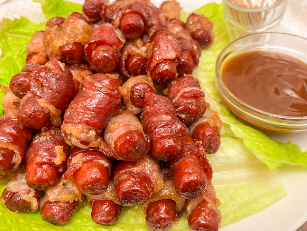 A platter of smokies resting on lettuce leaves with bbq dipping sauce.