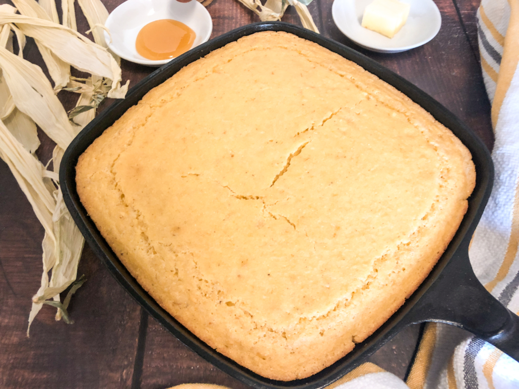 Fresh from the oven creamed corn cornbread still in the skillet with butter and honey in the background.