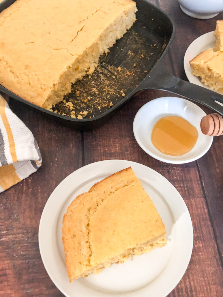 A slice of creamed corn cornbread on a plate with the dish of more in the background.