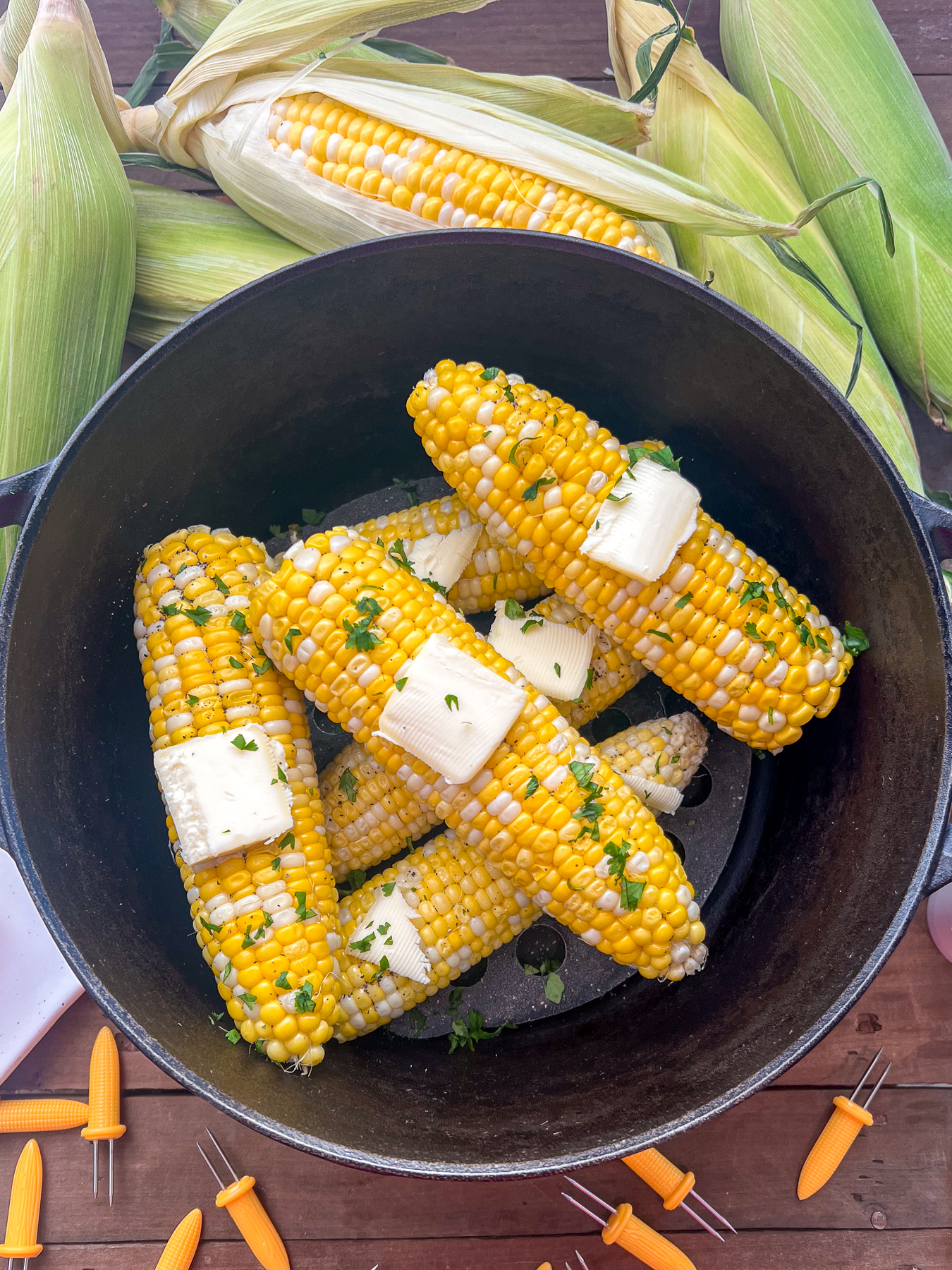 Steamed corn on the cob in a dutch oven with butter pats and parsley as garnish.