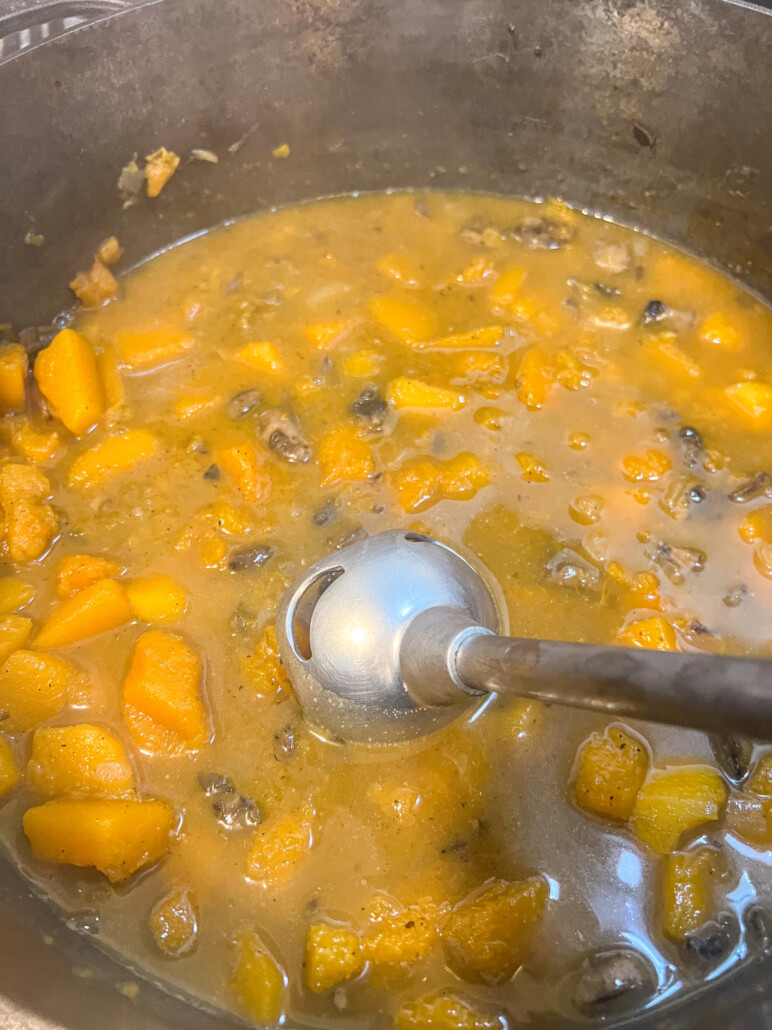 Once the butternut has fully cooked and softened, an immersion blender is pureeing everything to a thick soup base.