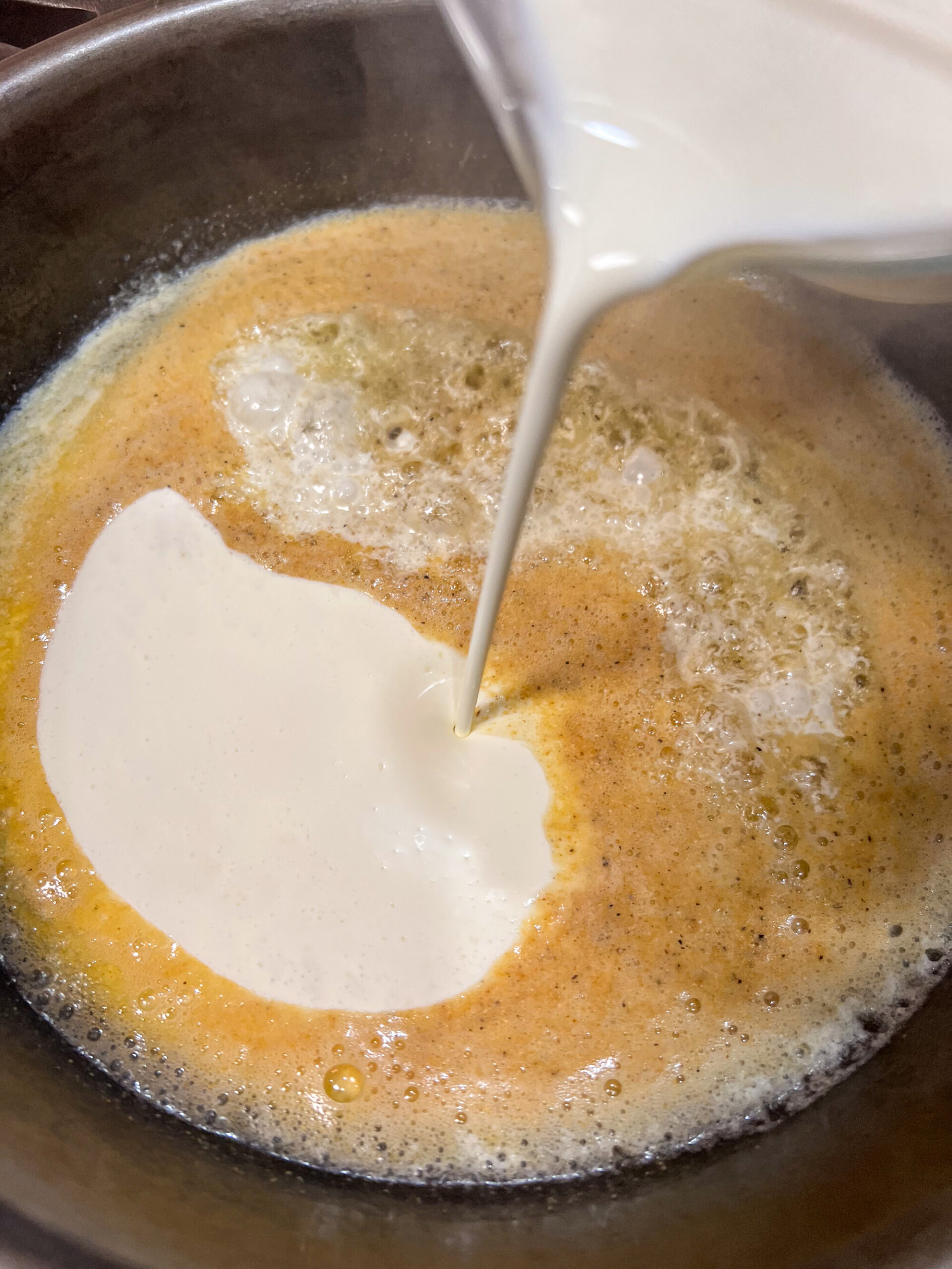 Seasonings and heavy cream added to the melted butter and olive oil in a cast iron skillet.
