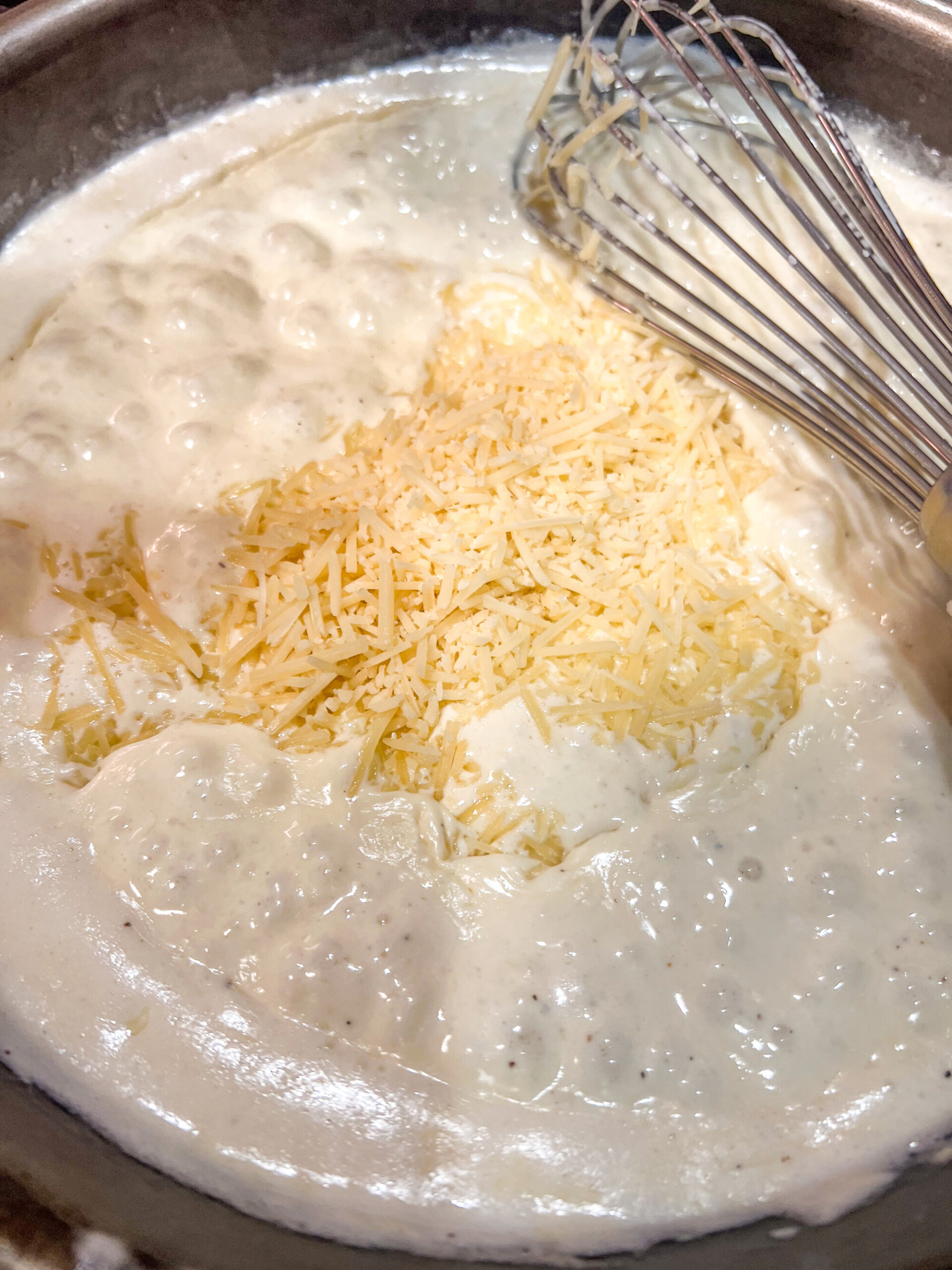 While simmering, the two cheeses are being added by the handful and whisked in to the creamy sauce.