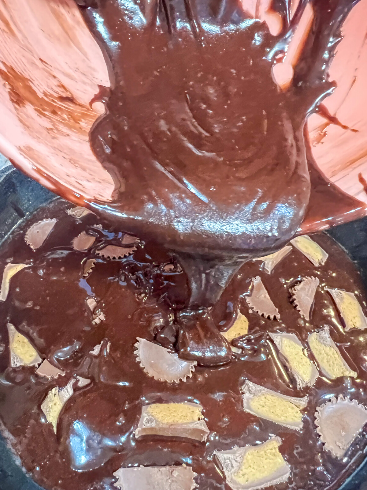 The remaining brownie batter being poured into the skillet to cover the candy.