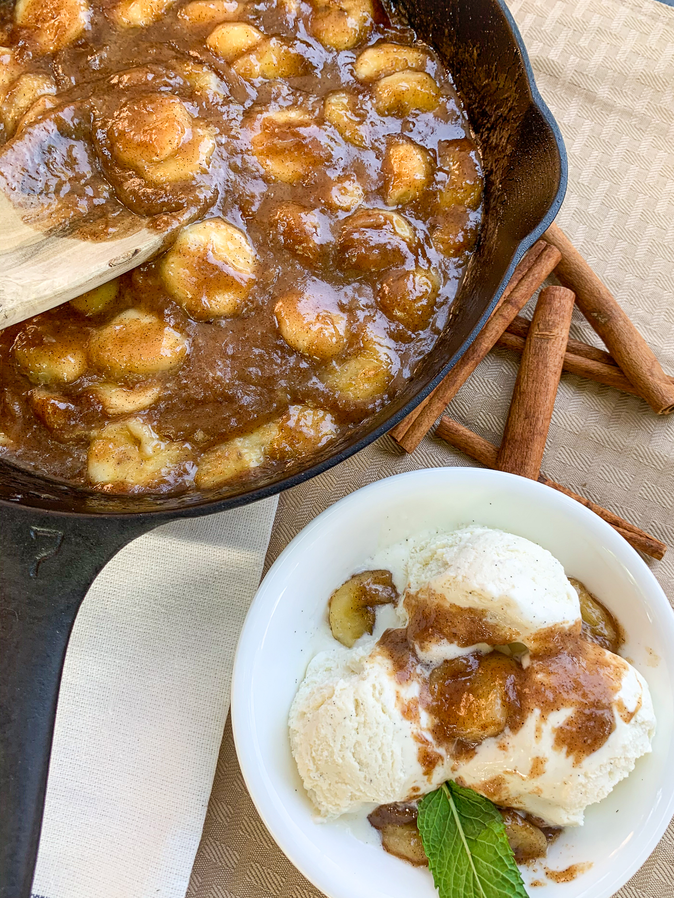 Skillet Bananas Foster ready to serve with one portion in a white bowl over ice cream.