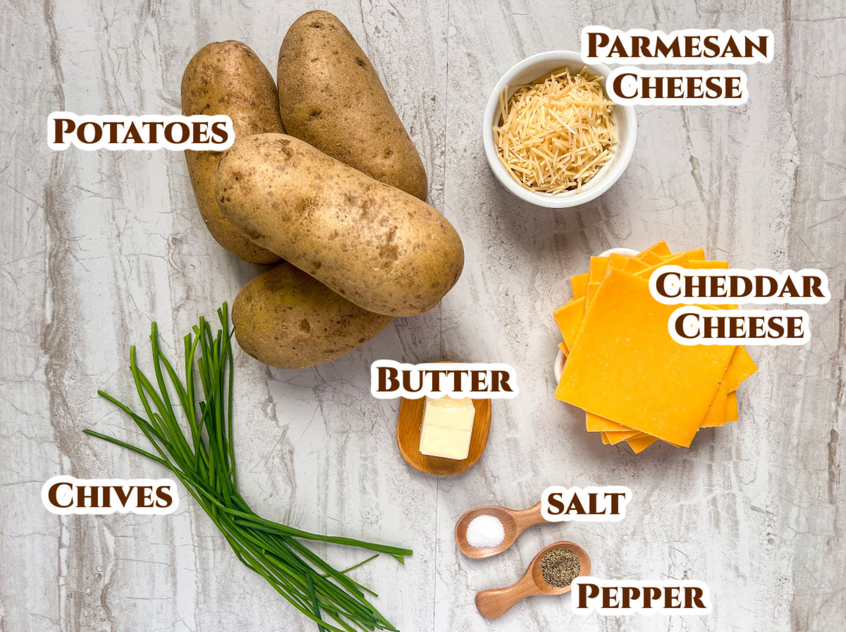 Ingredients to make cheesy hasselback potatoes in a cast iron skillet: russet potatoes, parmesan and cheddar cheese, butter, salt, pepper, and chives.