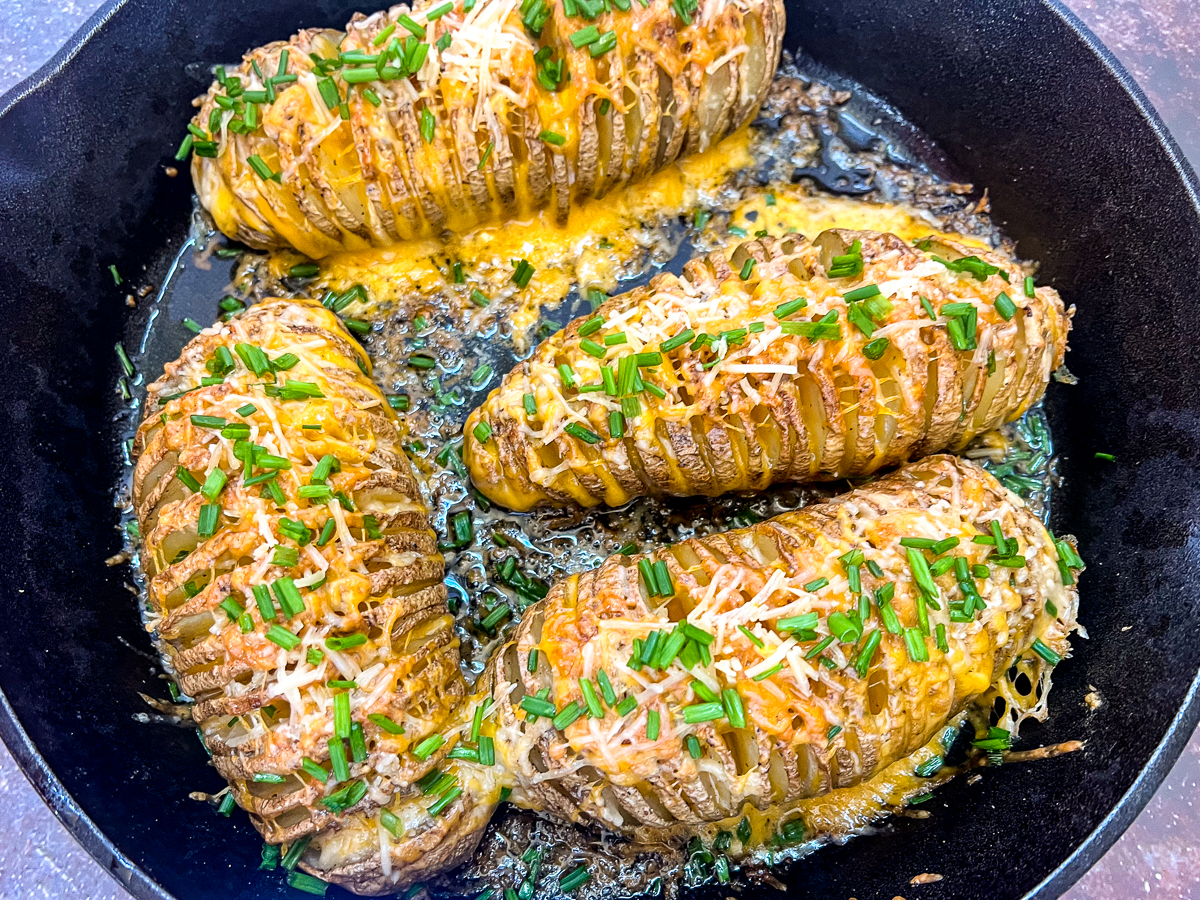 Cast iron skillet of freshly roasted cheesy hasselback potatoes with chives.