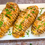 Three cheesy hasselback potatoes on a white platter.
