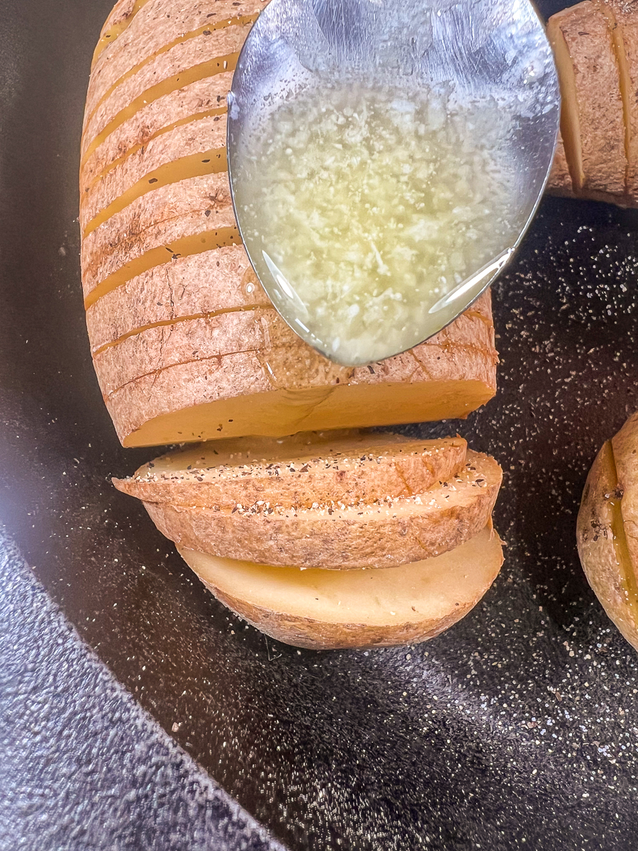 Melted butter being spooned between the layers of sliced potatoes.