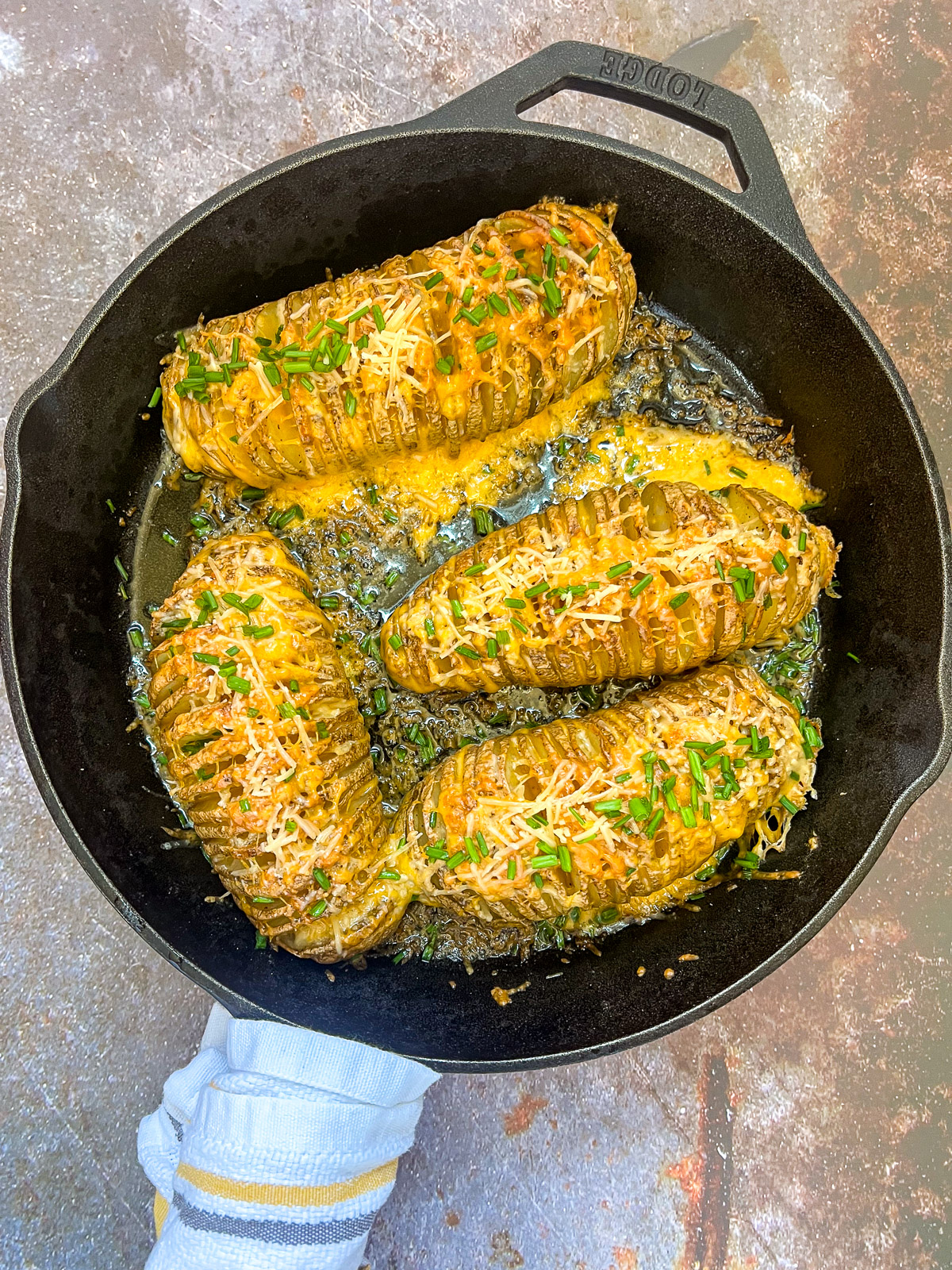 Four hasselback potatoes topped with two types of cheese and chives in a cast iron skillet.