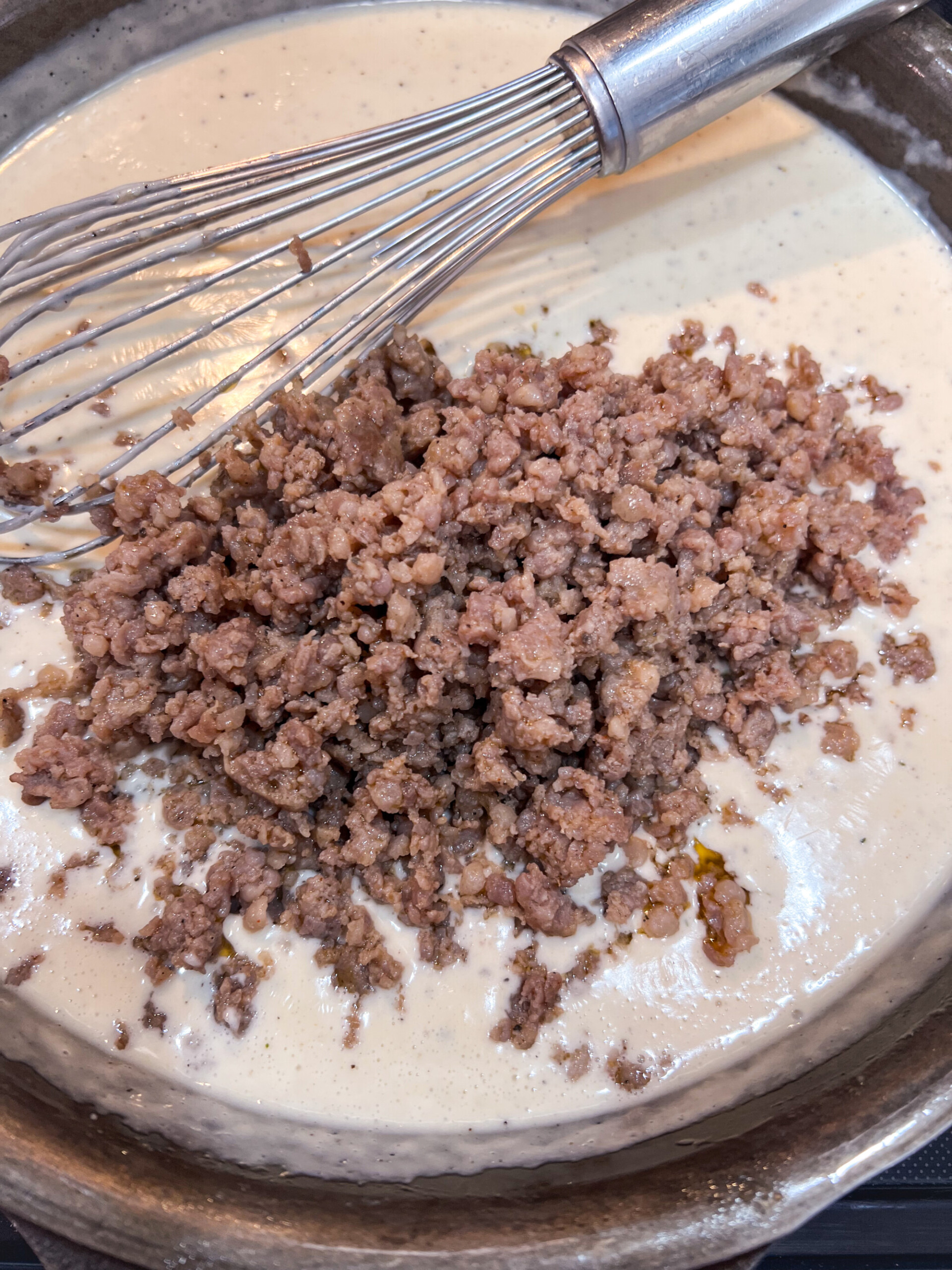 Breakfast sausage being added to the gravy in a cast iron skillet.