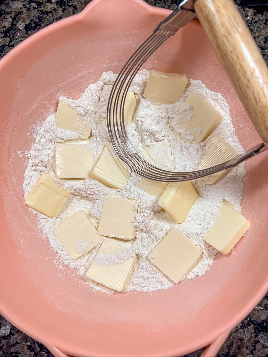 Dry ingredients with butter and a cutter in a bowl to make biscuits.