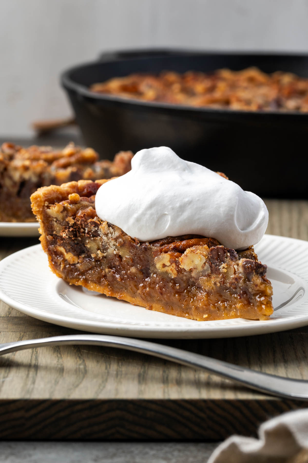 A slice of chocolate pecan pie on a plate topped with whipped cream.
