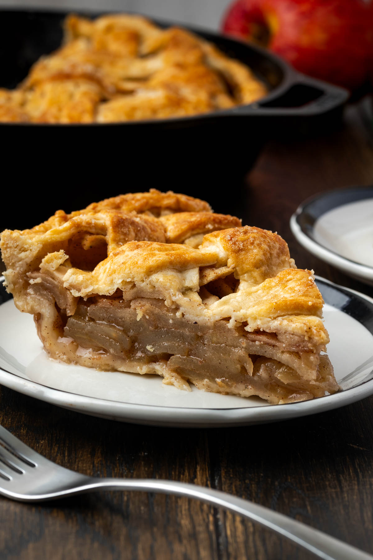 A slice of skillet apple pie on a late with the entire pie in the background.
