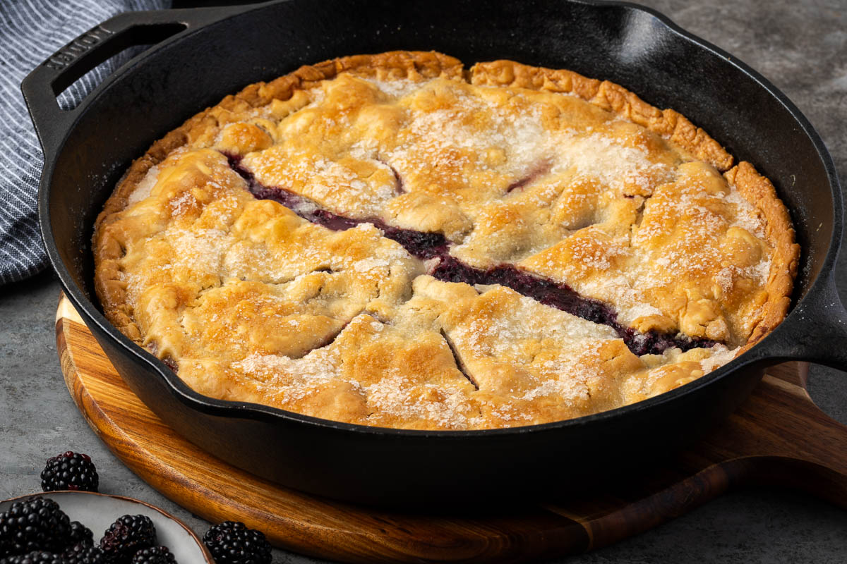 Baked southern blackberry cobbler on a table with fresh blackberries scattered around.