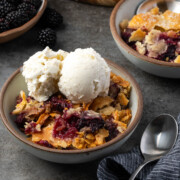 A serving of Southern blackberry cobbler in a bowl topped with vanilla ice cream.