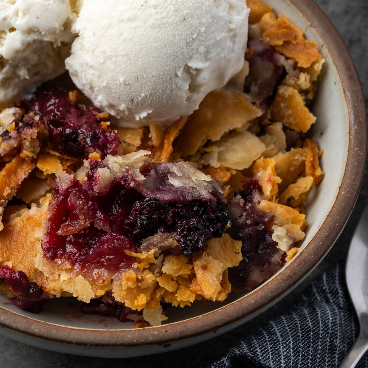 Southern blackberry cobbler with pie crust in a bowl with scoops of ice cream.