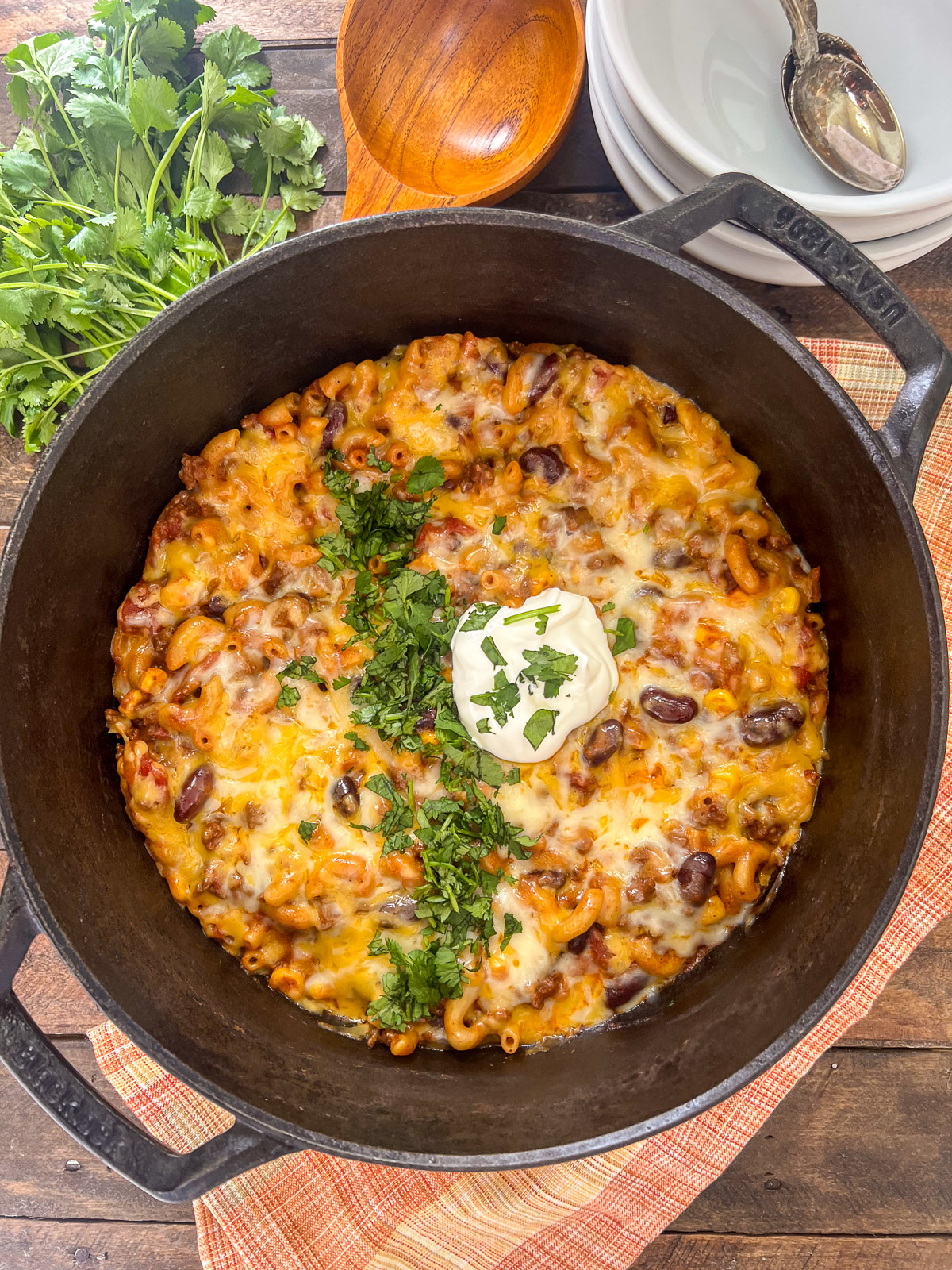 Easy cheesy chili mac in a dutch oven garnished with freshly chopped cilantro and a dollop of sour cream.
