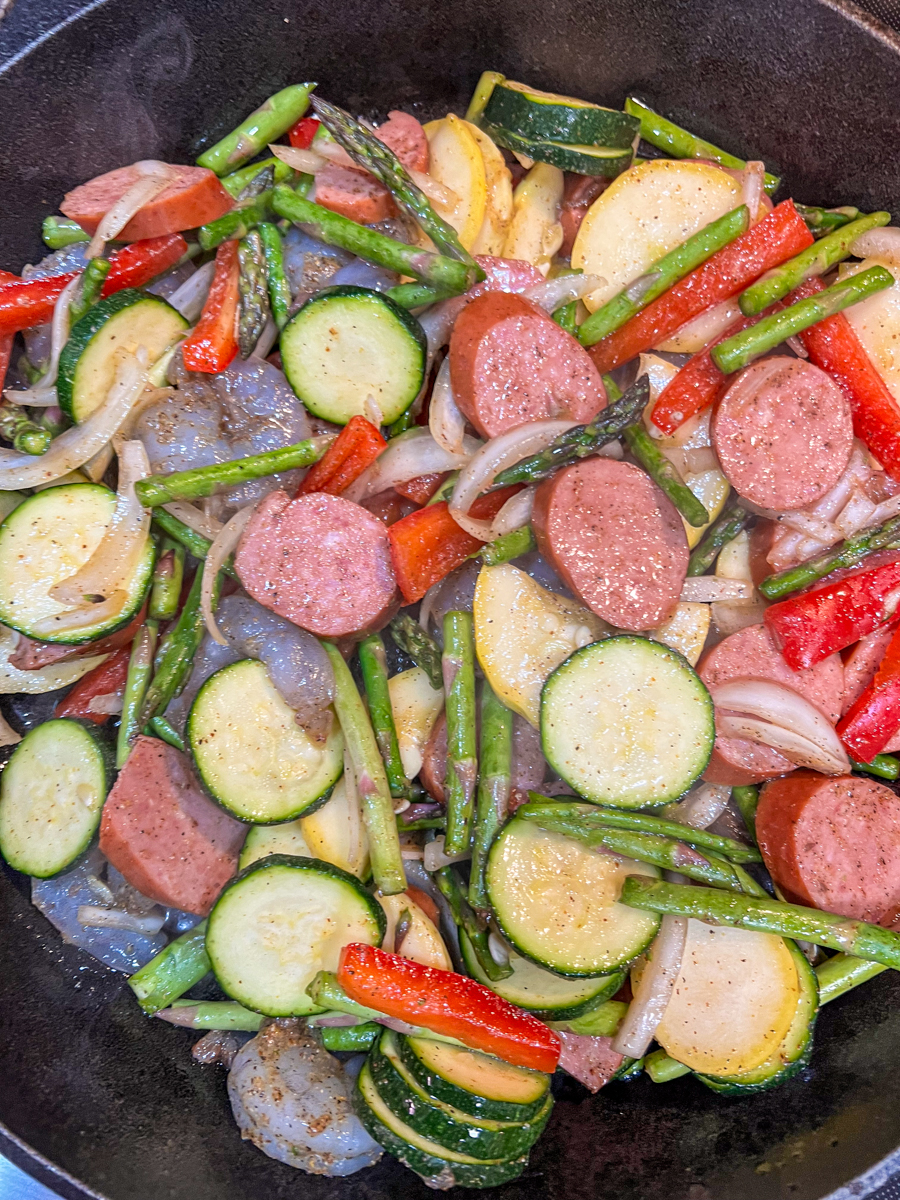 Shrimp and sausage cooking in a skillet with vegetables.