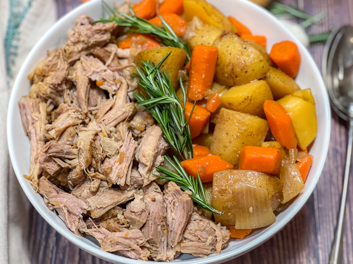 A serving bowl of pork pot roast with onions, potatoes, and carrots.