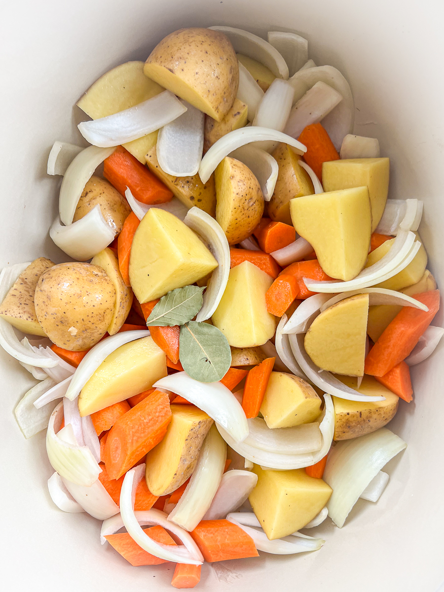 Potatoes, onions, carrots, and bay leaves have been added to the dutch oven.