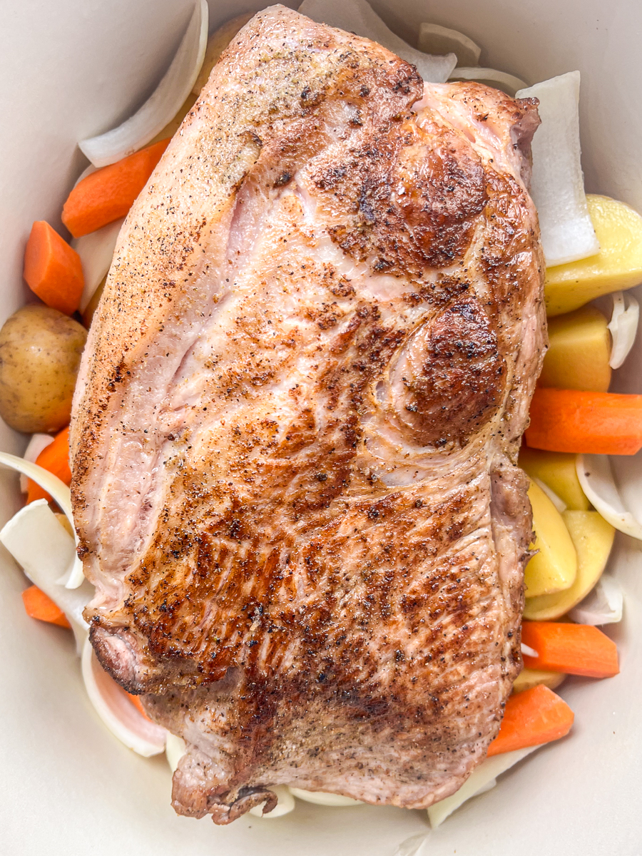 The seared pork roast is nestled into the vegetables in the Dutch oven.