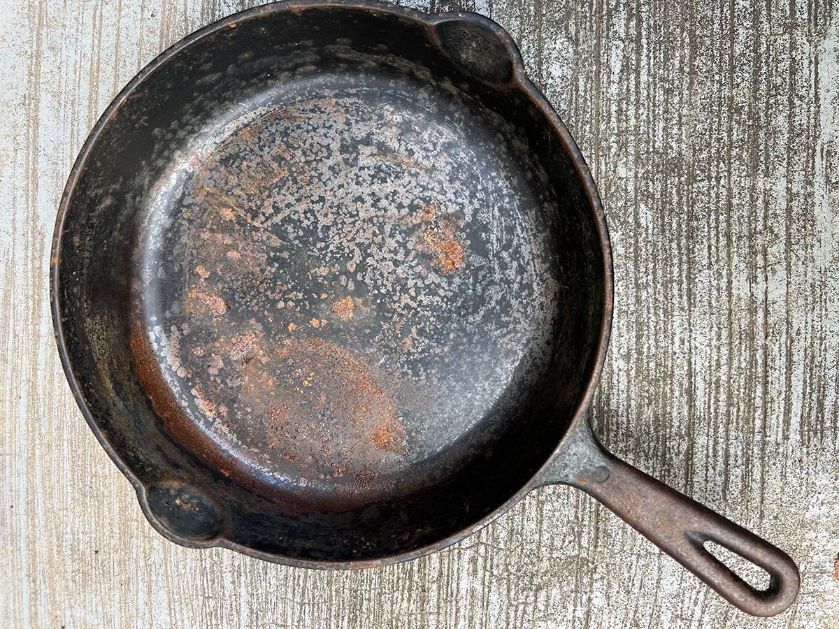 Rusted cast iron skillet on a wooden background.