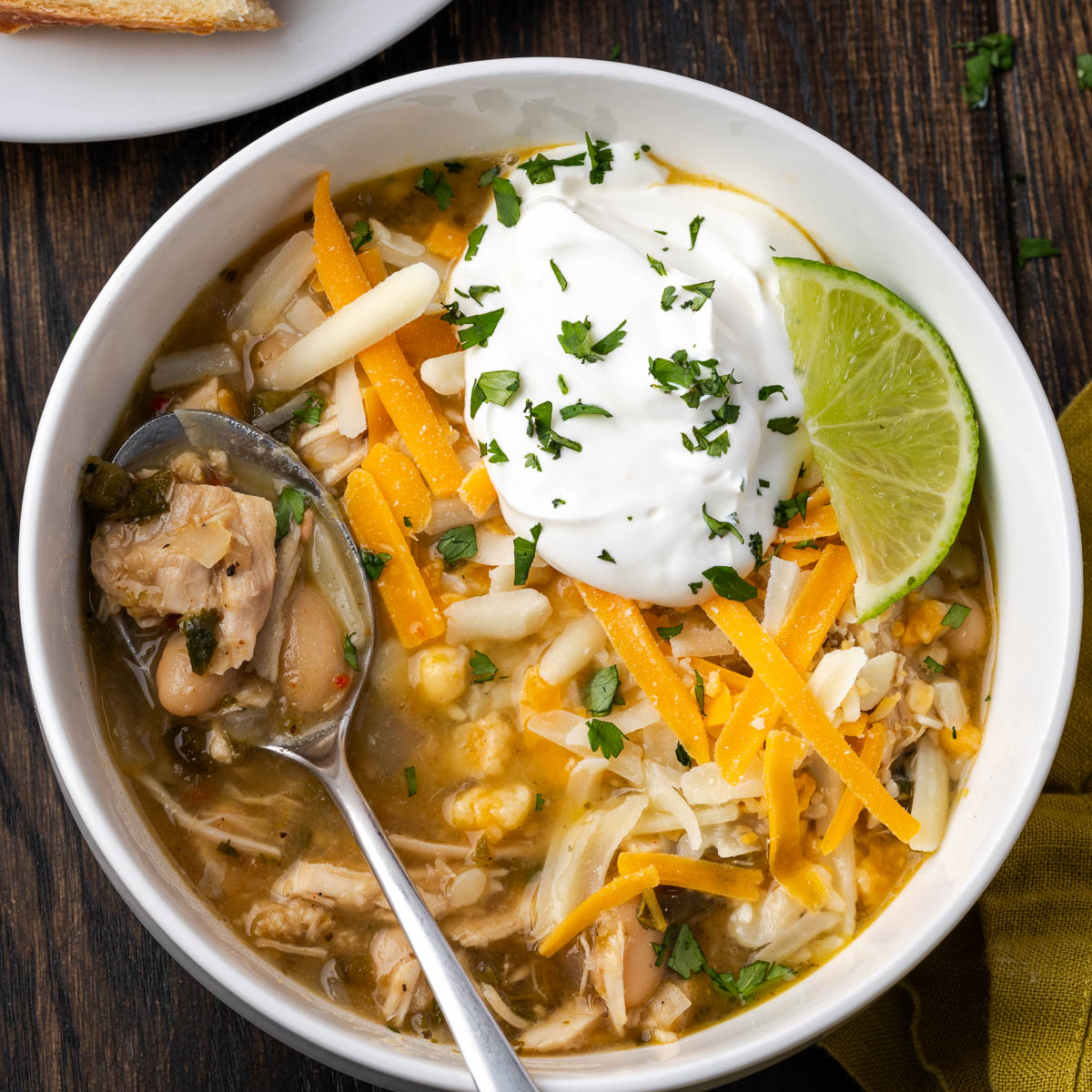 A bowl of Dutch oven white chicken chili topped with sour cream, cheese, and a lime wedge.