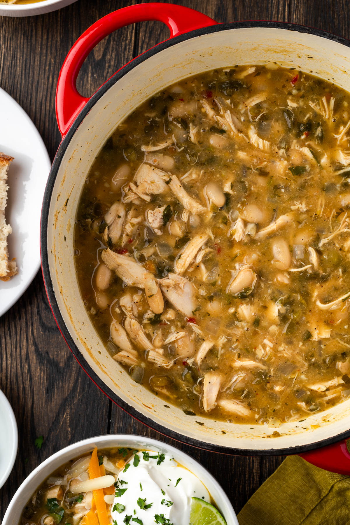 A bowl of Dutch oven white chicken chili with a bowl served up with toppigs.