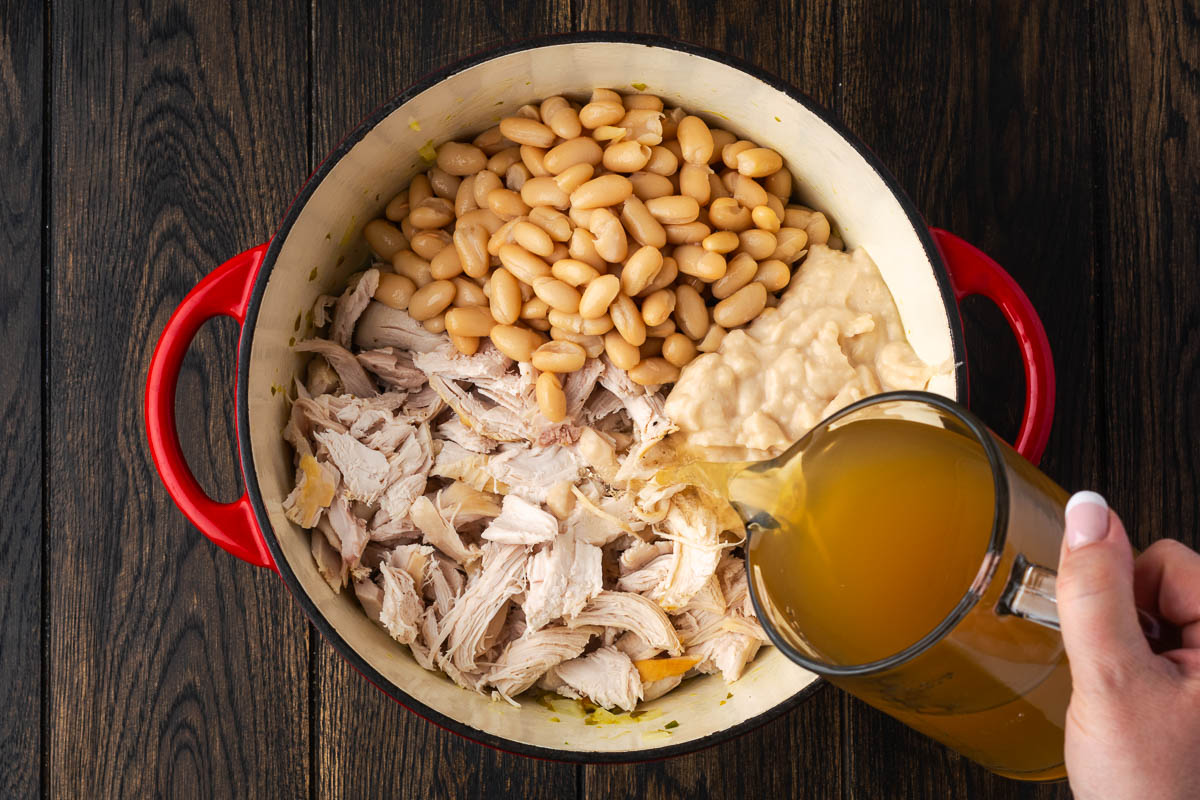 Beans and chicken added to the pot and broth pouring over the top from a glass pitcher.