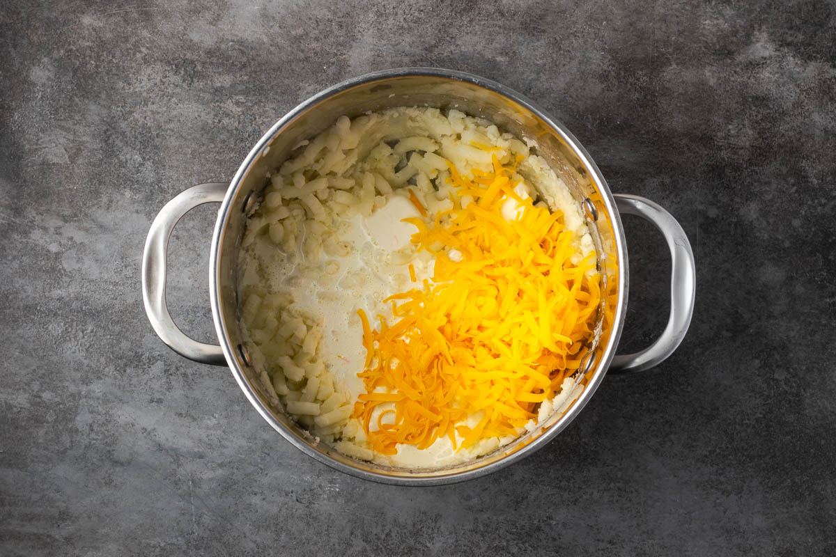 Mashed potato mixture in a pot with cheese and seasonings added. 