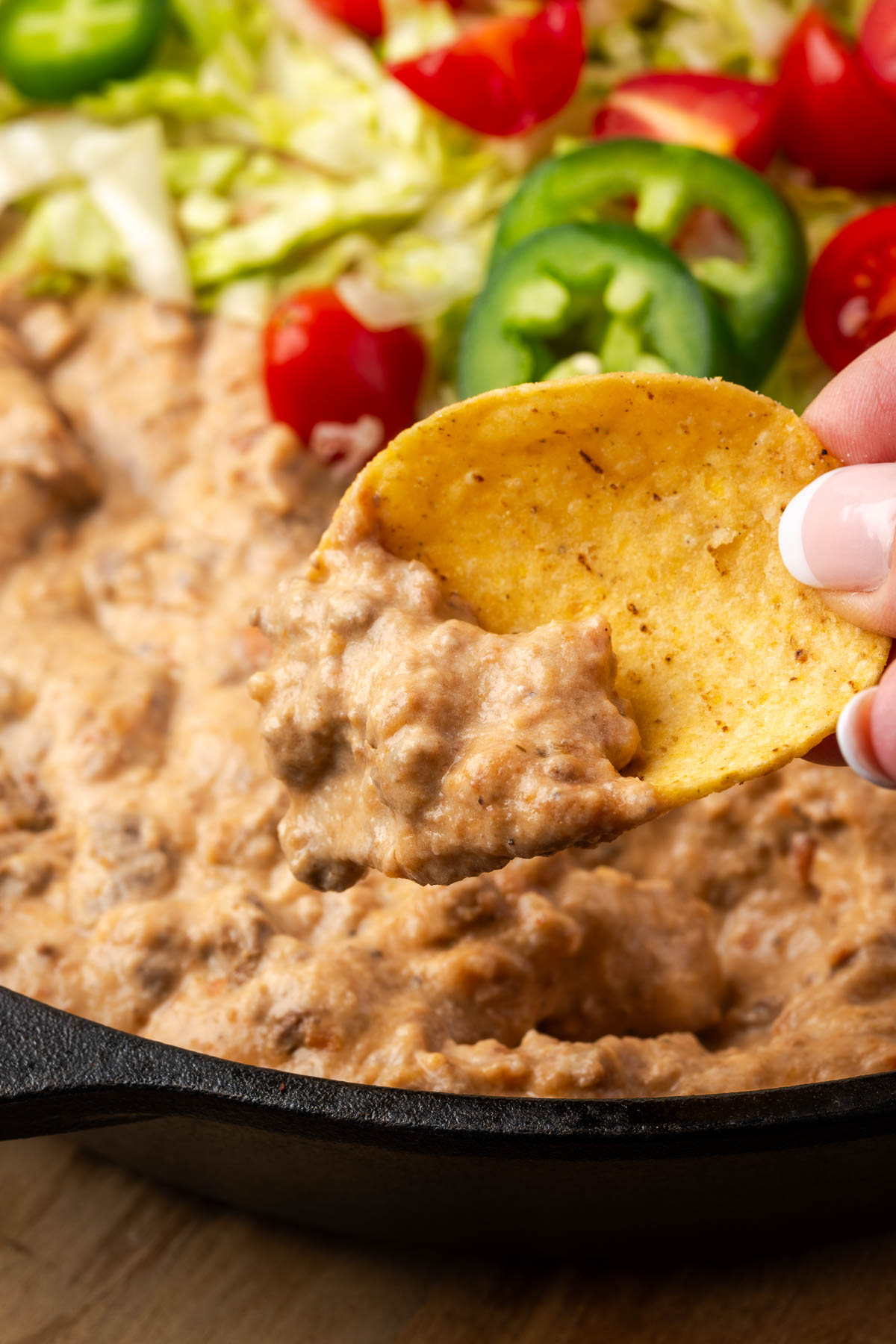 A hand scooping up a bit of nacho dip.