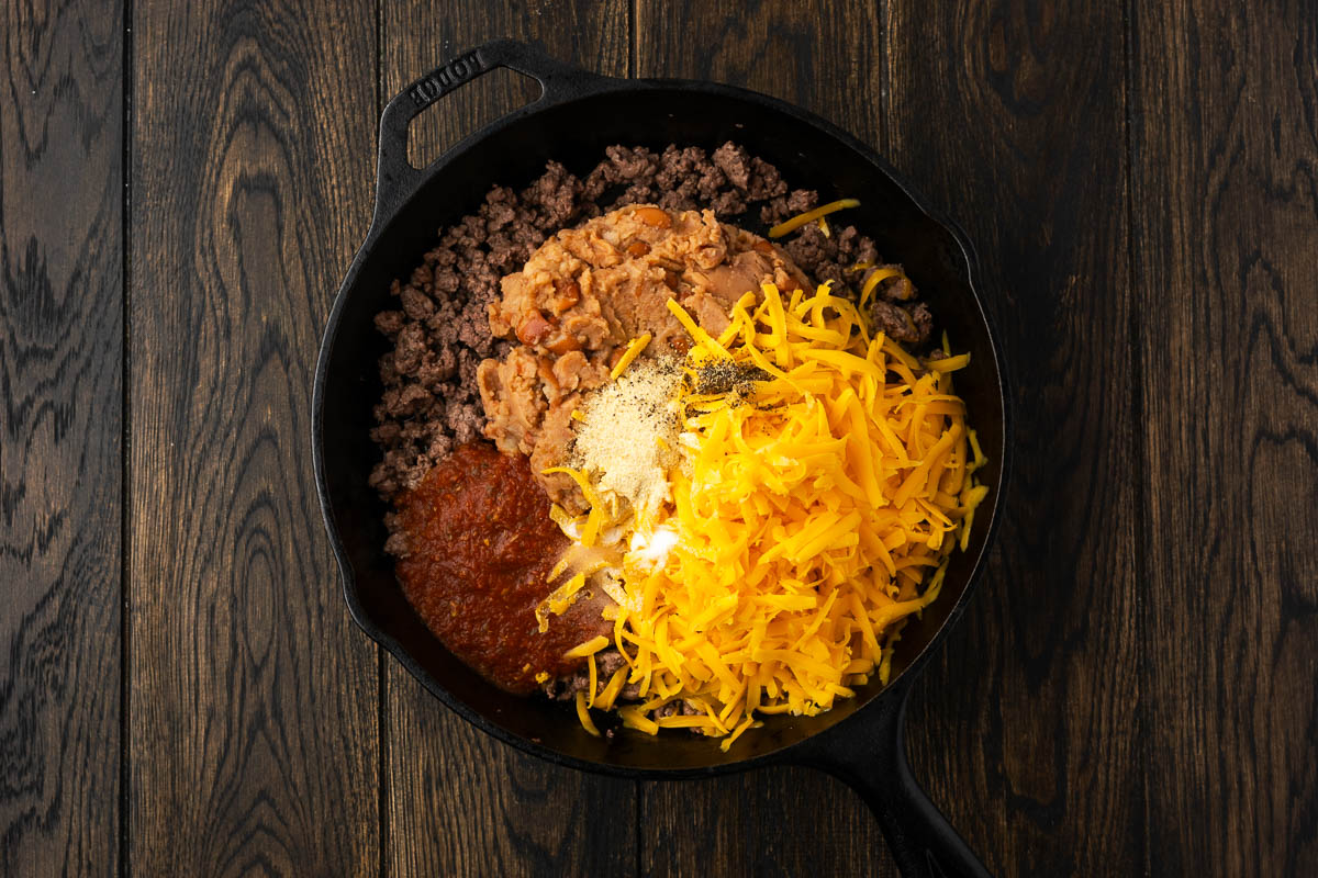 Cheese and other ingredients added to the beef in the skillet to make nacho dip.